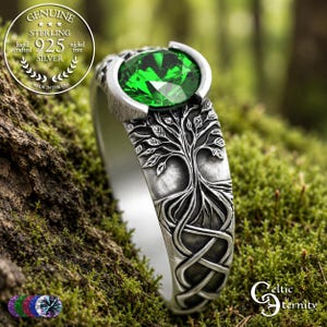 May include: A sterling silver ring featuring a round, faceted emerald green gemstone set in a bezel. The band displays an embossed tree of life design with intricate roots and branches. A circular seal reads Genuine Sterling 925 Silver.