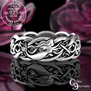 May include: A sterling silver ring with a Celtic knot design. The ring is nickel-free and hand-crafted in the USA. The ring has a detailed pattern with a dragon or serpent motif. The ring is reflected in a dark surface.