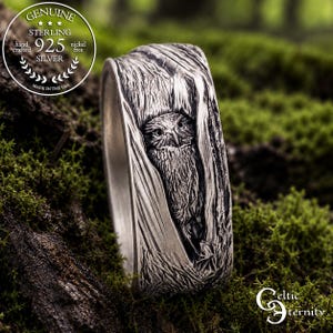 Puede incluir: Un anillo de plata de ley con una talla en relieve detallada de un búho anidado dentro de un patrón de corteza de árbol texturizado. La banda tiene un acabado oxidado para resaltar los detalles intrincados de las plumas y la veta.