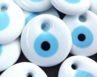 May include: A group of white ceramic charms with a blue and black evil eye design. Each charm has a small hole at the top for hanging.