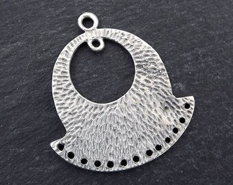 Puede incluir: Colgante de metal plateado con un acabado texturizado y martillado. El colgante presenta un gran círculo abierto en la parte superior, una base texturizada en forma de abanico y una serie de pequeños agujeros a lo largo del borde inferior. Ideal para bisutería.