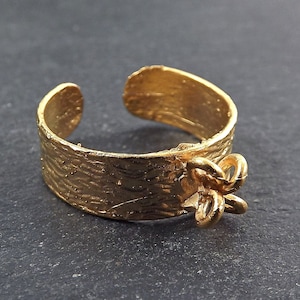 Puede incluir: Un anillo dorado con una banda texturizada y un adorno decorativo con forma de flor.