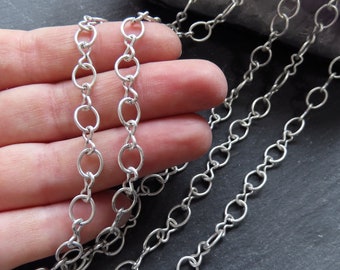 May include: Silver chain with oval links. The chain is shown in a hand, with multiple strands of the chain laid out on a dark surface.