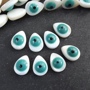 May include: A collection of teardrop-shaped, white mother of pearl beads with a turquoise blue eye and black pupil.