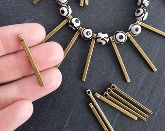 May include: A close-up of gold-colored metal jump rings. The jump rings are about 1 inch long and have a loop at each end. The jump rings are on a black surface.
