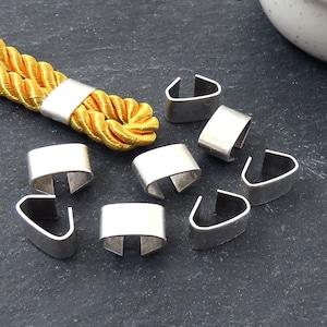 May include: Eight silver metal cord end caps, designed to secure the ends of cords or ropes. The caps have a U-shaped opening and are shown on a dark gray surface.