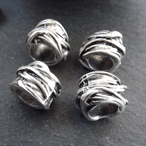 May include: Four silver metal beads with a textured, woven design. The beads are cylindrical and have a hole through the center.