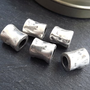 May include: Five silver metal beads with a hammered texture. The beads are cylindrical and have a hole through the center.