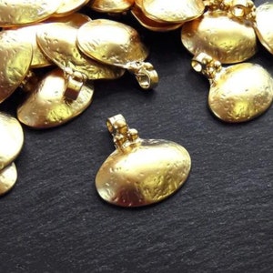 Puede incluir: Un montón de abalorios de metal de color dorado en forma de semicírculo. Los abalorios tienen una superficie texturizada y un pequeño bucle en la parte superior para sujetarlos a joyas.