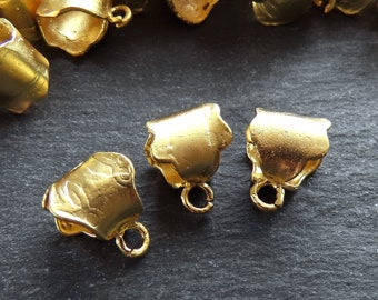 Op de afbeelding: Close-up van verschillende kleine, goudkleurige metalen belvormige kralen. Elke kraal heeft een lus aan de basis om te rijgen. De kralen zijn verspreid over een donker, getextureerd oppervlak. Deze kralen zijn ideaal voor het maken van sieraden.
