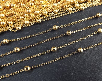 May include: Close-up of gold-colored chain necklaces with small, evenly spaced beads. The chains are arranged in parallel lines, with a pile of chains in the background. The chains have a shiny, metallic finish.