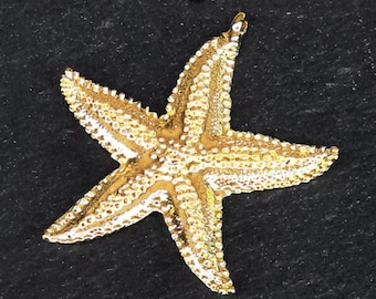 May include: A gold-coloured starfish ornament with a textured surface. The starfish is on a black background.