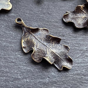 Op de afbeelding: Een verzameling antieke goudkleurige metalen eikenblaadjescharms. De bladeren hebben een gedetailleerd, getextureerd ontwerp en zijn perfect voor het maken van sieraden of knutselen.