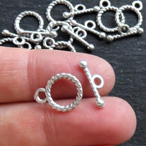 Puede incluir: Cierre de palanca de metal plateado con diseño de cuerda trenzada. Los cierres tienen un bucle redondo en un extremo y una barra con un bucle en el otro extremo.