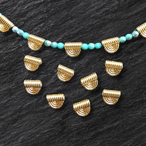 May include: Gold-toned metal bead caps with a decorative, ridged design. The bead caps are arranged on a black surface.