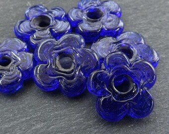 Op de afbeelding: Zes kobaltblauwe glazen bloemen kralen met een gat in het midden. De kralen zijn licht getextureerd en hebben een 5-bladige bloemvorm.