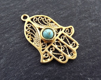 May include: Gold-toned filigree hamsa hand charm with a turquoise stone in the center.