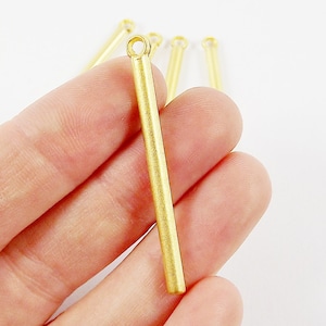 May include: Five gold metal bar pendants with a loop at the top. The pendants are about 1 inch long.