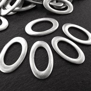 Puede incluir: Primer plano de seis anillos de salto ovalados de plata. Los anillos están dispuestos en forma de semicírculo sobre una superficie negra.