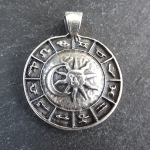 May include: Silver pendant featuring a circular zodiac wheel with the sun and moon in the center. The wheel is surrounded by the twelve zodiac signs.