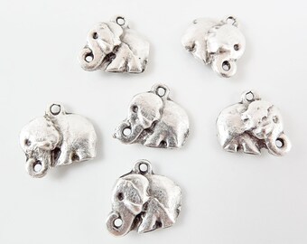 Puede incluir: Seis encantos de elefante de plata con un bucle para sujetar a joyas u otras artesanías. Los elefantes están mirando hacia la derecha y tienen la trompa levantada.