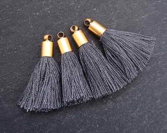 May include: Four gray tassel ornaments with gold metal tops. The tassels are made of a soft, fuzzy material.