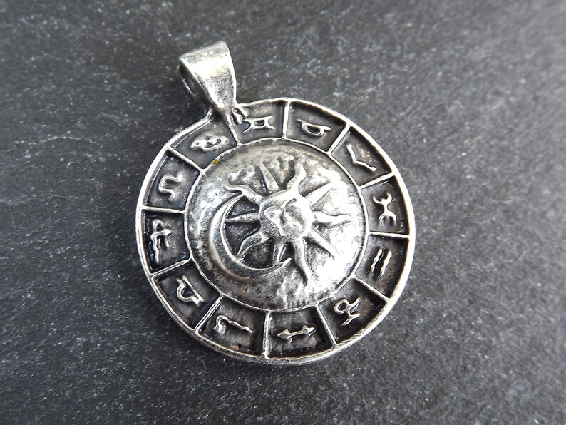 May include: Silver pendant featuring a circular design with the zodiac symbols and a sun and moon graphic.
