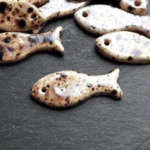 May include: A group of ceramic fish ornaments with a speckled brown and white glaze. The fish are all different sizes and shapes, and they have a hole in the top for hanging.