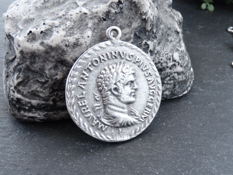 May include: Silver pendant featuring a Roman emperor bust with the inscription "IMP ANTONINVS PIVS AVG" around the edge.