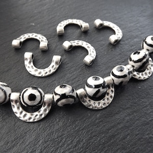May include: A set of silver-toned metal beads with a hammered texture and black and white patterned glass beads. The beads are strung on a clear cord.