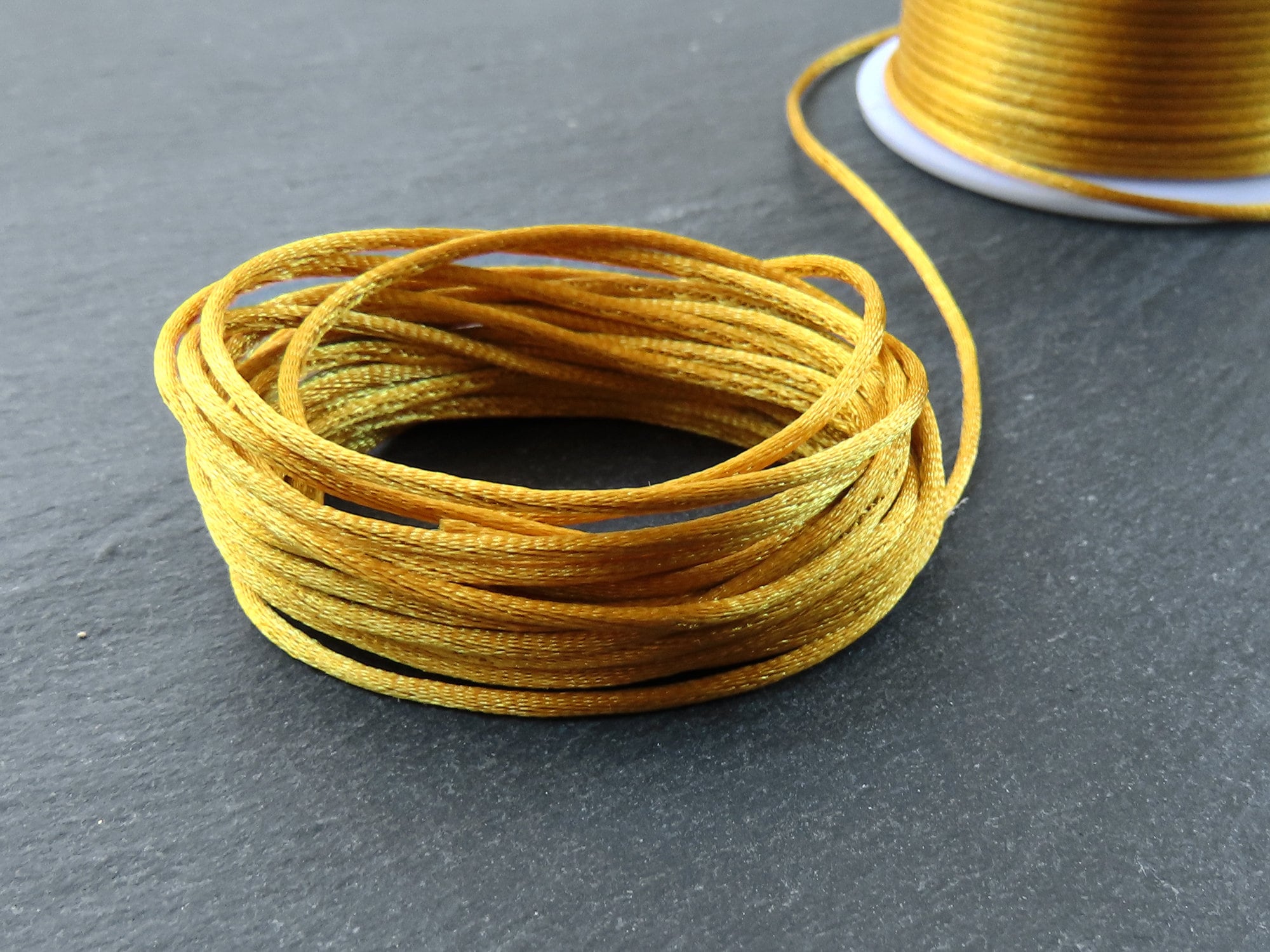 Cord, imitation silk, gold, 1mm. Sold per 100-foot spool. - Fire Mountain  Gems and Beads