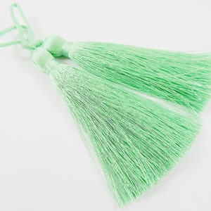 May include: Two light green tassel ornaments with a loop at the top for hanging.