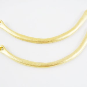 May include: Two gold-colored metal hoops with a smooth finish and rounded edges. Each hoop has a small hole at the top.