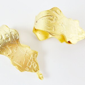 Puede incluir: Dos colgantes de metal de color dorado con dise&ntilde;os intrincados. Los colgantes tienen forma de hojas y una superficie texturizada.