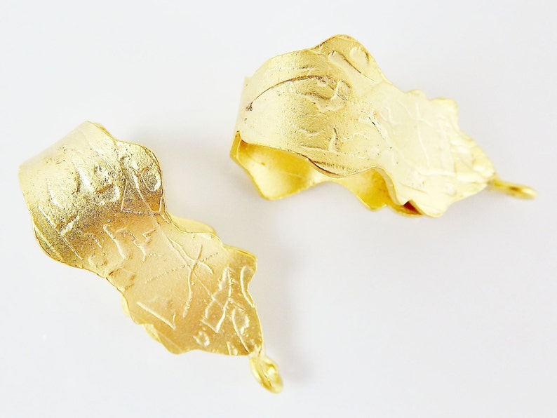 Puede incluir: Dos colgantes de metal de color dorado con dise&ntilde;os intrincados. Los colgantes tienen forma de hojas y una superficie texturizada.
