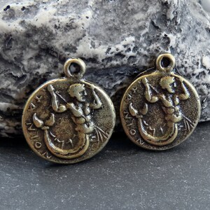 May include: Two antique gold-toned metal charms featuring the astrological sign Scorpio. Each charm depicts a stylized image of a scorpion with a human torso.
