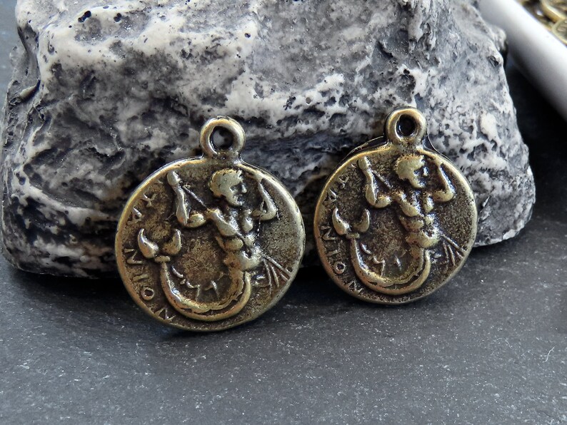 May include: Two antique gold-toned metal charms featuring the astrological sign Scorpio. Each charm depicts a stylized image of a scorpion with a human torso.
