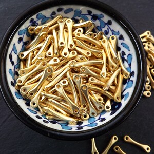 May include: A bowl filled with gold-colored metal beads. The beads are shaped like a slightly curved line with a small loop at each end. The bowl has a blue and white floral pattern.