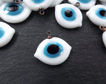 May include: A collection of white glass evil eye charms with blue and black centers. The charms have a copper loop for hanging.