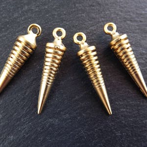 May include: Four gold-colored metal cone-shaped pendants with a spiral design. The pendants have a loop at the top for attaching to a chain or cord.