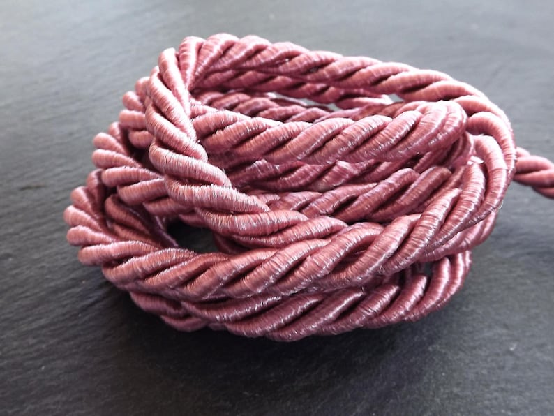 May include: A close-up of a pink twisted cord made of a soft, silky material. The cord is coiled and twisted, creating a textured and intricate pattern.
