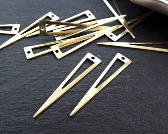 May include: A group of gold-colored metal triangle shapes with a hole at the top. The triangles are arranged in a random pattern on a black surface.