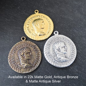 May include: Three round metal pendants with a Roman emperor's profile image and inscription. The pendants are available in 22k matte gold, antique bronze, and matte antique silver.