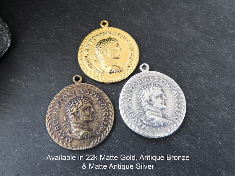 May include: Three round metal pendants with a Roman emperor's profile image and inscription. The pendants are available in 22k matte gold, antique bronze, and matte antique silver.