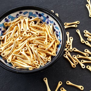 May include: A bowl filled with gold-colored metal beads. The beads are shaped like a small, elongated 'X' with a loop at each end. The bowl is white with blue and gold floral designs.