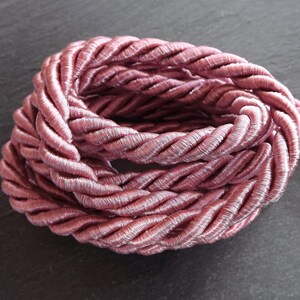 May include: A close-up of a pink braided rope. The rope is made of a soft, silky material and has a delicate, feminine look.