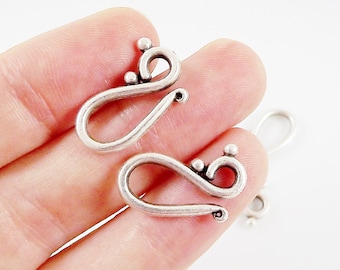 May include: Two silver-toned metal clasps with a decorative design. The clasps are shaped like a sideways 'S' with a small ball at the top of each curve.