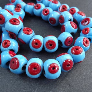 Op de afbeelding: Een streng blauwe glazen kralen met rode cirkels. De kralen zijn rond en hebben een glanzende afwerking.