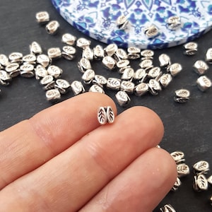 May include: Silver leaf-shaped beads, perfect for jewelry making or crafting projects. The beads are small and have a delicate design.