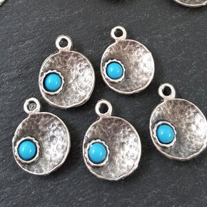 May include: Five silver-toned metal charms with a hammered texture and a turquoise blue cabochon stone in the center of each charm.